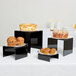 A group of three black acrylic risers with muffins on them.
