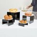 American Metalcraft black acrylic risers holding plates of cakes and muffins on a table.