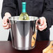 A person holding a silver Vollrath wine bucket with a bottle of wine inside.