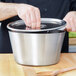 A person using a wooden spoon to stir a silver Vollrath bain marie pot.