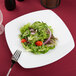 A Sushia super white porcelain square salad plate with salad and a fork.