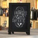 A Flash Furniture black magnetic tabletop chalkboard with metal scrolled legs on a white table.