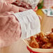 A person's hand using a Choice 70% Alcohol Antiseptic Moist Towelette to pick up chicken wings.