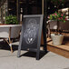 A Flash Furniture Canterbury vintage black wood A-frame chalkboard advertising a restaurant on a sidewalk.