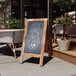 A Flash Furniture Canterbury vintage rustic brown wood A-Frame chalkboard sign on a sidewalk.