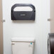 A San Jamar black pearl toilet seat cover dispenser on a wall above a toilet.