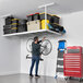 A man holding a bicycle above a SafeRacks overhead storage shelf with storage boxes.