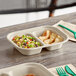 A World Centric compostable fiber container with two compartments of food on a table.
