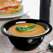 A Carlisle black melamine nappie bowl filled with soup with a spoon next to it.
