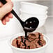 A black Fineline disposable ladle scooping chocolate ice cream into a white bowl.