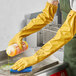 A person wearing Showa yellow knit-lined rubber gloves using a bottle of cleaning liquid.