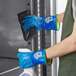 A person wearing blue Showa thermal insulated gloves cleaning a refrigerator.
