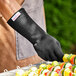 A person wearing a Mr. Bar-B-Q black quilted cotton oven / grill glove holding a skewer of food.