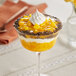 A glass bowl of dessert with mango filling topped with whipped cream.