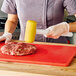 A person in gloves using a Carlisle yellow mallet to tenderize meat on a cutting board.