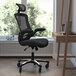 A black Flash Furniture office chair in front of a desk with a laptop and pen.