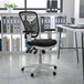 A Flash Furniture black mesh office chair with adjustable arms and a white frame at a black and white desk.