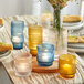 A table with a group of Acopa clear glass tealight holders with lit candles and flowers on it.