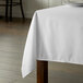A rectangular white Intedge tablecloth on a wooden table.