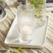 A tealight candle in a clear ribbed glass holder on a tray.