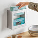 A person putting gloves in a stainless steel double box glove dispenser on a kitchen counter.