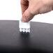 A hand using a white San Jamar Oceans lever roll towel dispenser to put a white object in a black box.