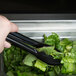 A person holding a Carlisle black plastic utility tong to a salad.