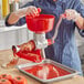 A woman using a Tre Spade red stainless steel manual tomato squeezer with a plastic bowl to make tomato sauce.
