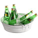 A round galvanized metal tub filled with green bottles of beer on ice.