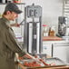 A man using a Tre Spade stainless steel vertical sausage stuffer on a counter in a butcher shop.