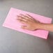 A hand using a Chicopee pink foodservice wet wiper to wipe a counter.