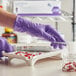 A person in a purple Kimtech gloves cutting pills on a tray.