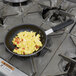 A Carlisle aluminum non-stick fry pan with scrambled eggs on top of a stove.