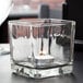 A Libbey glass cube votive holder with a lit candle inside.