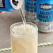 A person pouring Stubborn Agave Vanilla Cream Soda into a glass with a straw.