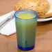 A Cambro Del Mar Sapphire Blue plastic tumbler filled with yellow juice next to a bagel on a table.