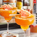 Two glasses of orange liquid with grapefruit garnish on a bar.