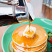 A person using a Tablecraft Modern Glass Syrup Dispenser to pour syrup over a stack of pancakes.