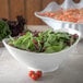 A Carlisle white oval bowl filled with salad with green and red leaves and tomatoes.