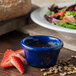 A blue Carlisle ramekin filled with sauce and seeds next to a salad.