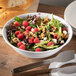 A Carlisle white melamine bowl filled with salad with raspberries and nuts.