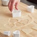 A person using white Ateco plastic heart shaped cookie cutters.