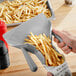 A person using a Choice plastic dual handle French fry scoop to pour fries onto a tray.