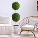 Two LCG Sales artificial double ball boxwood topiary shrubs in faux stone pots next to a chair.