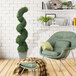 An LCG Sales artificial spiral topiary shrub in a faux stone pot in a room with a green chair and a stool.