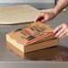 A person opening a Choice kraft corrugated pizza box on a table.