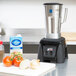 A Waring commercial blender on a counter with a stainless steel container of food.