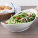 A white porcelain canoe bowl filled with salad next to a basket of bread.