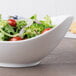 A 10 Strawberry Street white porcelain canoe bowl filled with salad on a wood table.