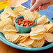 A hand dipping a Tostitos Crispy Rounds tortilla chip into a bowl of salsa.